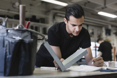 Young high school student writing in book while holding metal in training class