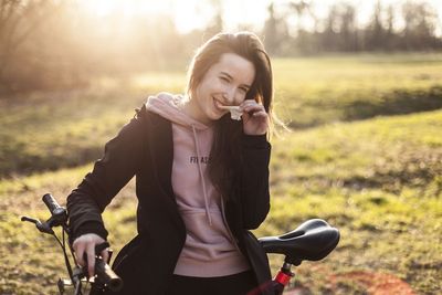 Portrait of smiling young woman with bicycle standing in park
