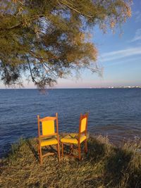 Empty chair on shore by sea against sky