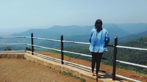 Full length of woman looking at view while standing by railing against mountains