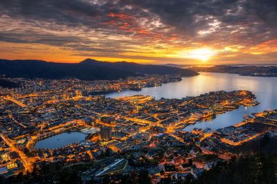 Aerial view of illuminated cityscape against cloudy sky during sunset