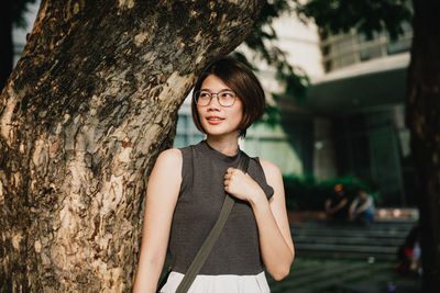 Portrait of a smiling young woman standing against tree trunk