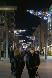 People walking on illuminated street amidst buildings in city at night