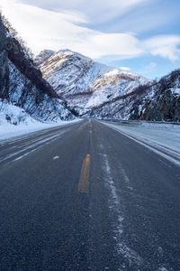 Road amidst snowcapped mountains against sky during winter