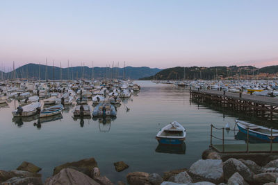 Boats moored in harbor at sunset