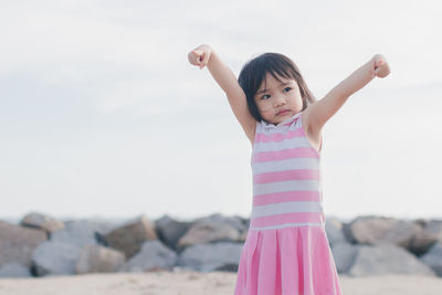 Cute girl with arms raised standing at beach against clear sky