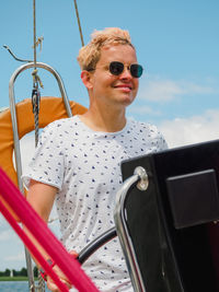 Smiling young man steering wheel on sailboat or yacht during summer sailing trip person