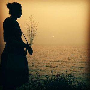 Silhouette woman standing by sea against sky during sunset