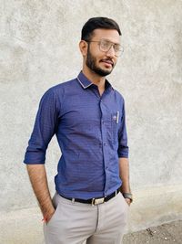 Young man looking away while standing against wall