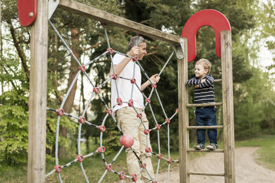 Boy looking at father climbing jungle gym at playground