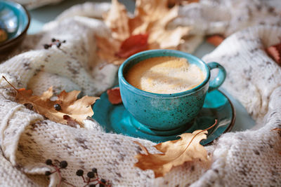 White knitted scarf, blue cup of coffee and dry yellow leaves