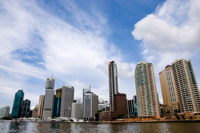 Modern buildings by river against sky in city