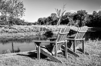 Empty chairs by lake against sky