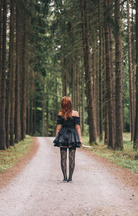 Rear view of woman walking on road in forest