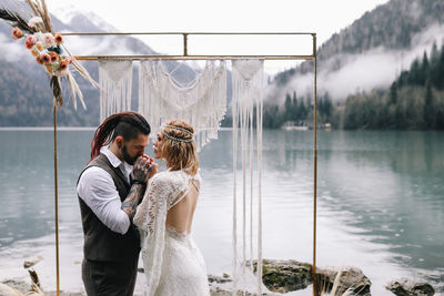 A loving married couple the bride and groom in suits celebrate wedding near the mountains and water