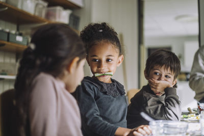 Multiracial female students eating cucumber by male classmates in day care center