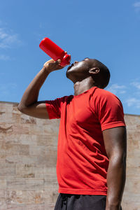 Low angle of thirsty african american athletic male drinking fresh water from plastic bottle during training on sunny day in city