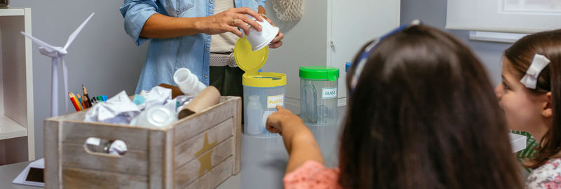 Girl pointing recycle box while female teacher holding plastic pack