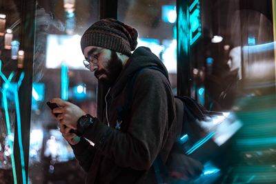 Man looking at camera while standing in illuminated city during winter