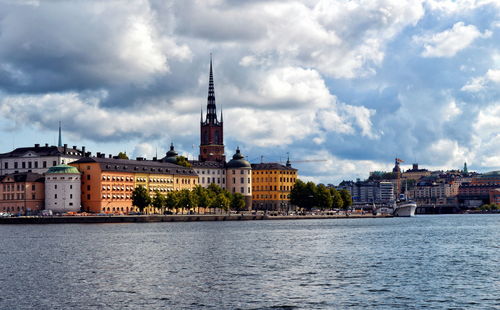 Buildings at waterfront against cloudy sky