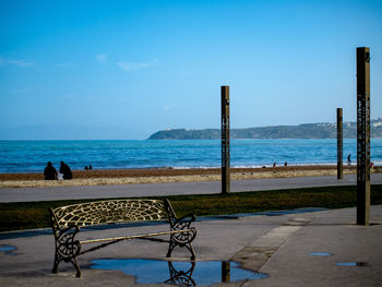 Empty bench on beach against sky