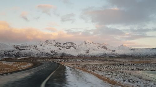 Road by snowcapped mountains against sky during sunset