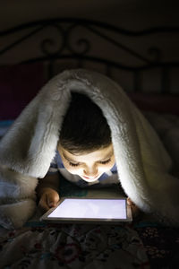 Little child using a tablet covered with a blanket