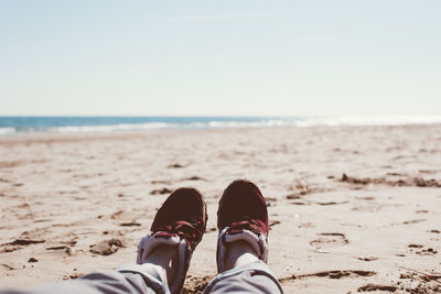 Low section of person with shoes on beach during sunny day