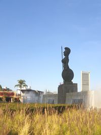 Statue on field against clear blue sky