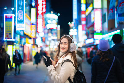 Portrait of young woman standing on illuminated street at night