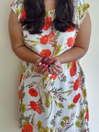 Midsection of woman holding red standing against wall