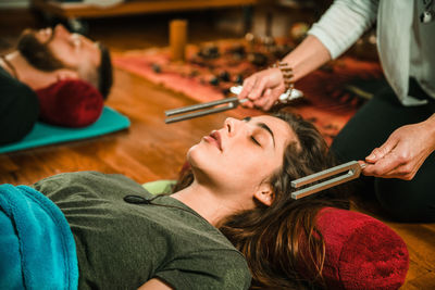 Therapist holding equipment by young woman while performing music therapy at spa