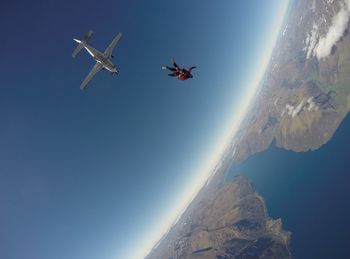 Fish-eye lens shot of person falling from airplane towards landscape and sea