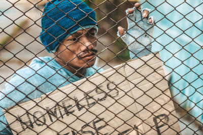 Portrait of young man looking through chainlink fence