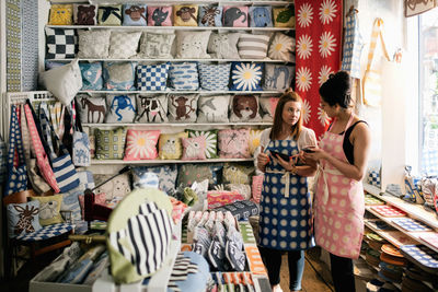 Female owners talking while holding smart phone and digital tablet in fabric shop