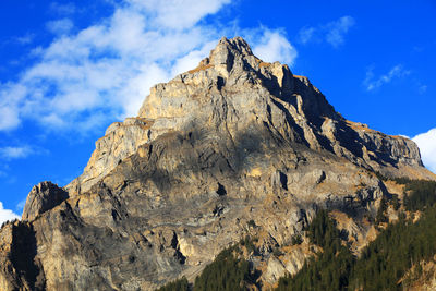 Low angle view of rocky mountain against cloudy sky