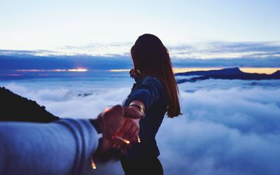 Cropped image of man holding girlfriend hand by cloudscape