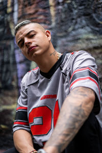 Portrait of young man sitting against graffiti wall