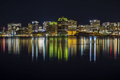 Illuminated buildings by river against sky at night