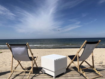 Chairs on beach by sea against sky