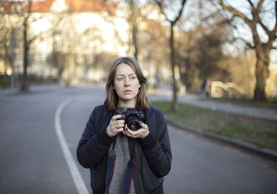 Portrait of young woman photographing against trees