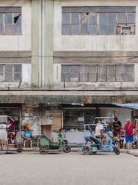 People and tricycles on street against building in city