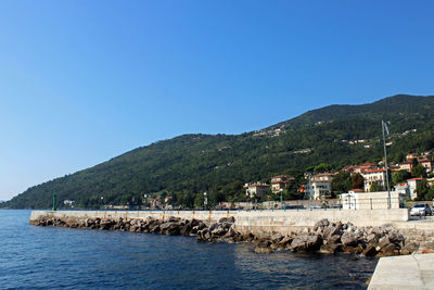 Scenic view of sea by buildings against clear blue sky