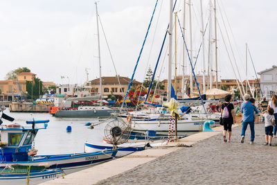 Rear view of people walking on footpath by boats moored at harbor