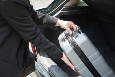 Pretty young brunette putting suitcase in car trunk before going on vacation