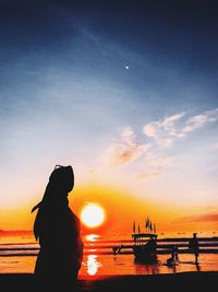 Silhouette woman standing by sea against sky during sunset