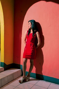 Full length of woman standing against red wall