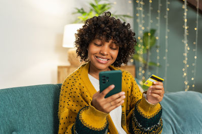 Young woman using mobile phone while sitting on sofa at home