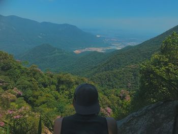 Rear view of man wearing cap looking at mountains against clear blue sky