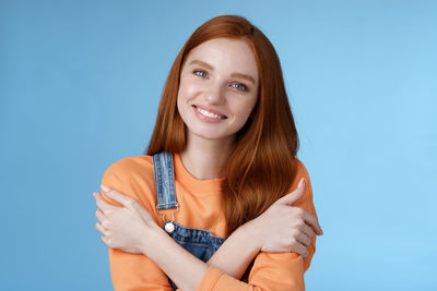 Cute woman hugging self against blue background